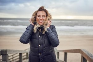 Lachende Frau mittleren Alters bei windigem Wetter am Strand