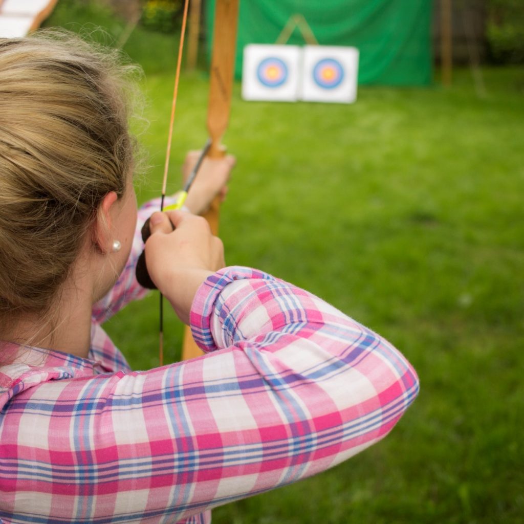junge Frau zielt auf Zielscheibe mit Pfeil und Bogen