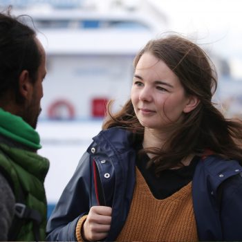 junge Frau mit Rucksack in einem Hafen im Gespräch mit einem jungen Mann