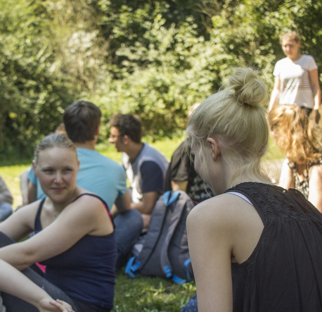 Junge Menschen sitzen auf Wiese und unterhalten sich