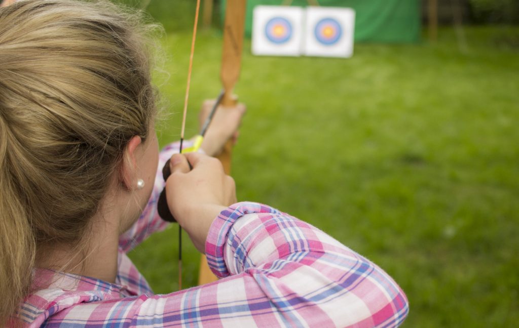junge Frau, die mit Pfeil und Bogen auf eine Zielscheibe zielt
