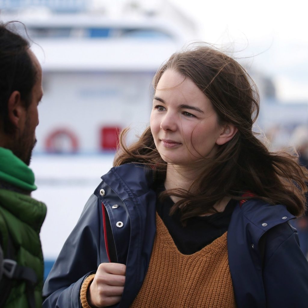junge Frau mit Rucksack in einem Hafen im Gespräch mit einem jungen Mann